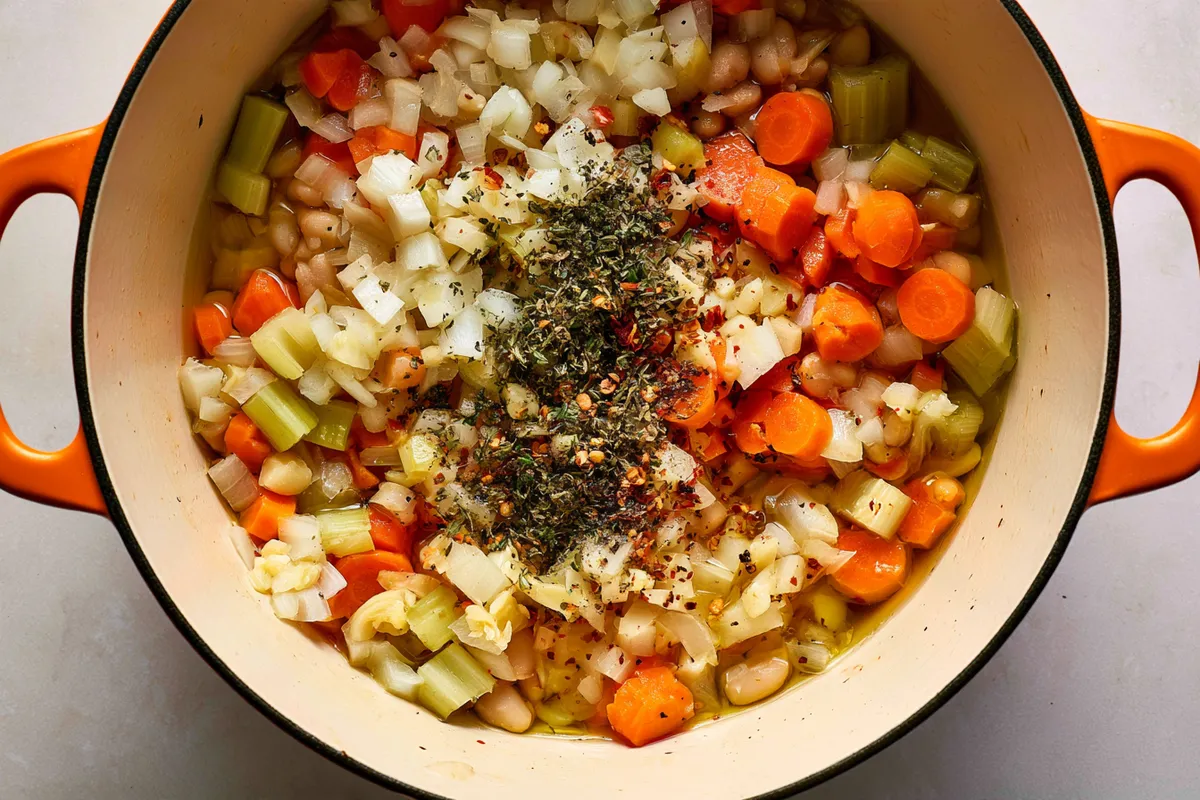 High Fiber Chicken Soup with White Beans and Artichokes 2 High fiber chicken soup in progress in a wide Dutch oven, with diced onion, sliced carrots, celery, garlic, oregano, thyme, and red pepper flakes glistening in olive oil as they soften