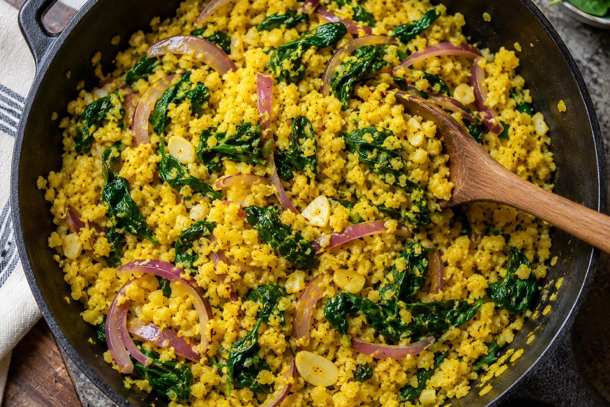 Honey Chili Salmon High Protein and Fiber Dinner Bowls 3 Overhead skillet scene for high protein and fiber dinner bowls, showing turmeric-yellow cauliflower rice with red onion, garlic, and wilted green spinach being stirred with a wooden spoon