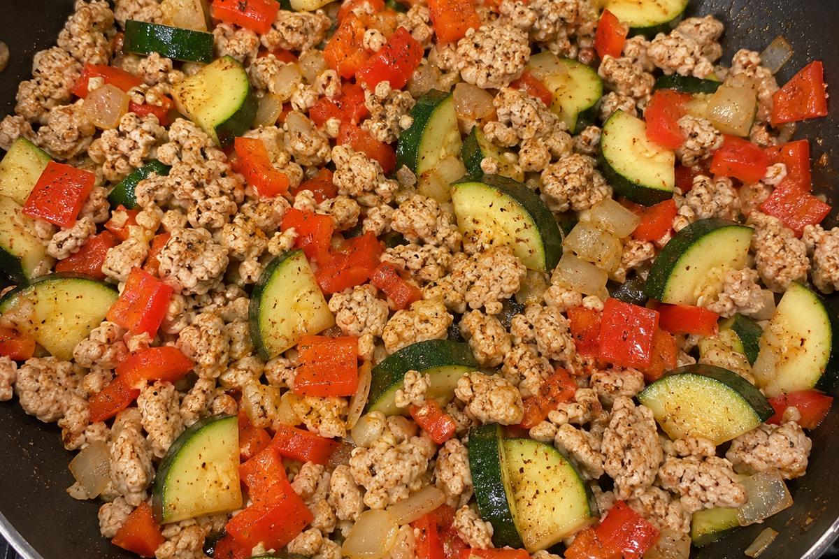 Low Calorie High Protein High Fiber Dinner: Smoky Turkey Bean Skillet 2 Close overhead view of a low calorie high protein high fiber dinner in progress, with lean ground turkey crumbles, softened zucchini, diced red bell pepper, onion, and garlic cooking in a large nonstick skillet
