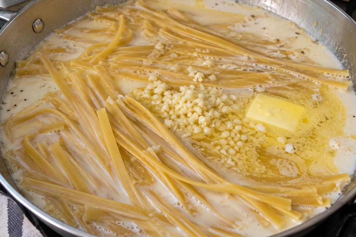 One Pot Garlic Parmesan Pasta 2 One pot garlic parmesan pasta at the beginning of cooking in a wide skillet, with fettuccine strands softening in milk and chicken broth around minced garlic and melted butter